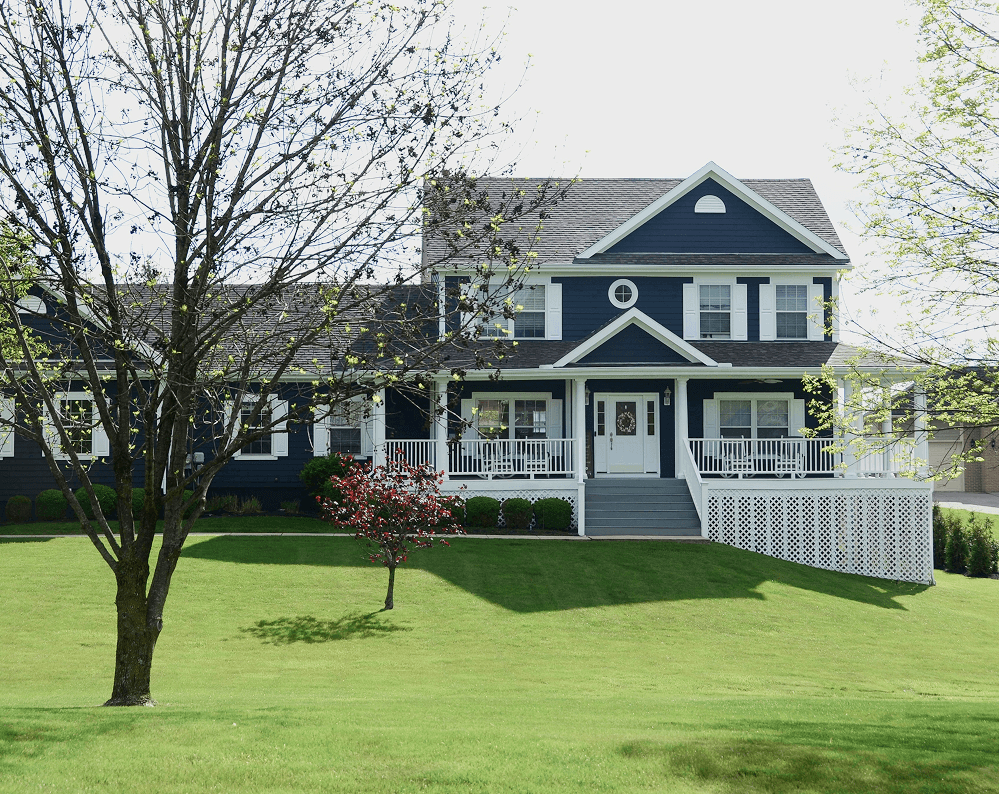 Navy farmhouse with a spring lawn and a blooming red tree